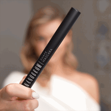 Una mujer de ojos azules con un vestido blanco aplicándose Shape Mascara